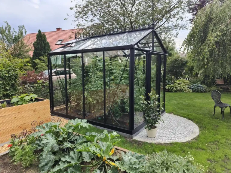 Ein modernes Gewächshaus im Garten mit Pflanzen, daneben Hochbeet. HOGATEK von Hof und Garten Wittstock.